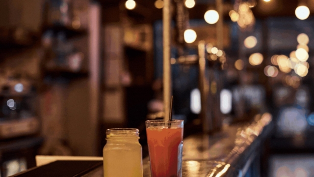 An image focusing on two cocktails on a bar. One is yellow and one is pink.