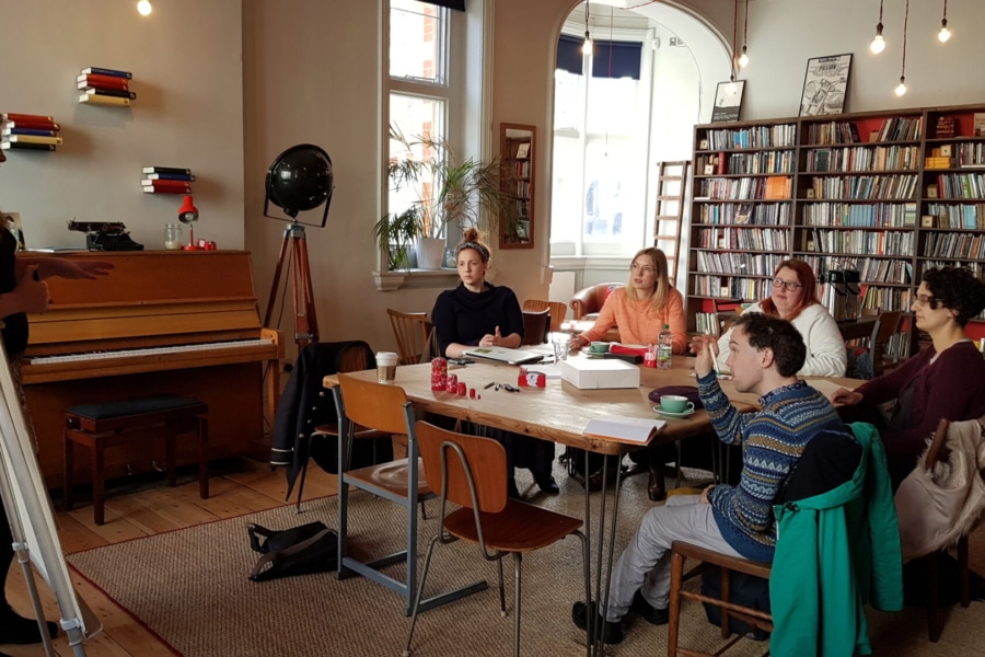 writers group of people sat in the library watching someone stood at the front, presenting to the group.