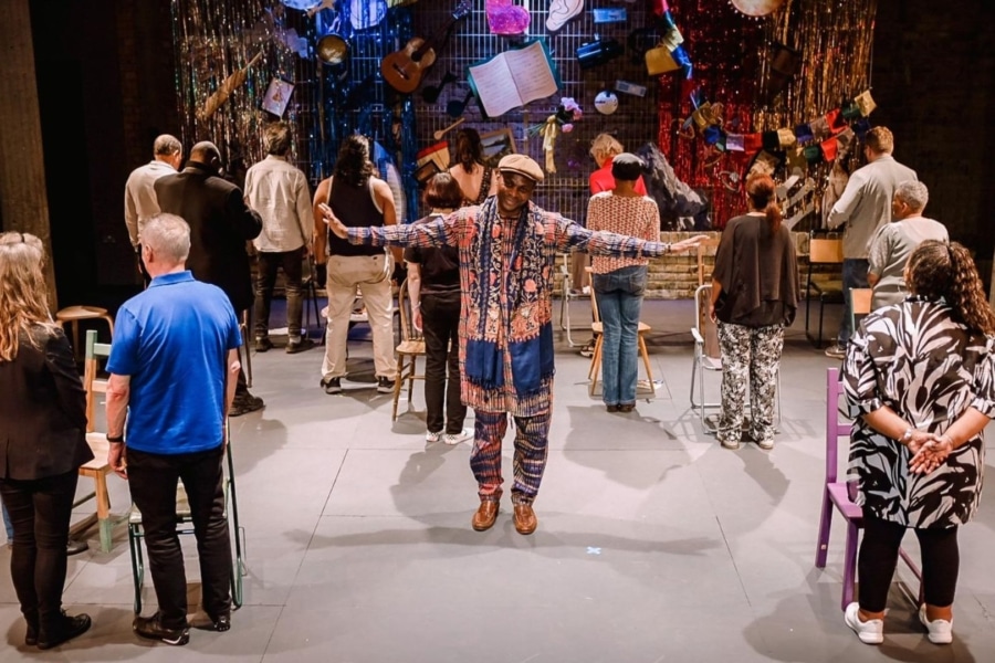 group of people on stage. One person is facing the camera with their arms outstretched, the other people are facing the other way.