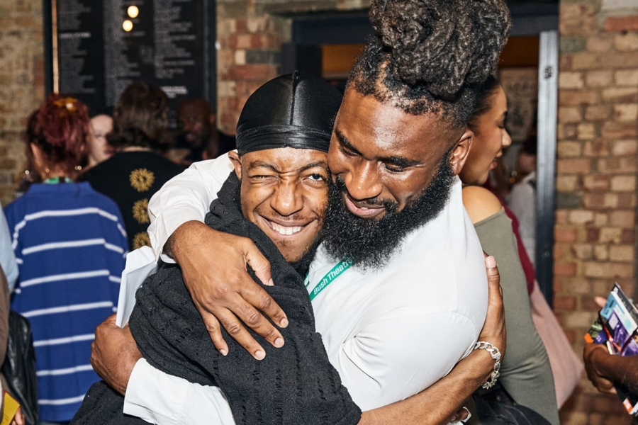 A group of people looking happy. Two men are hugging whilst smiling.