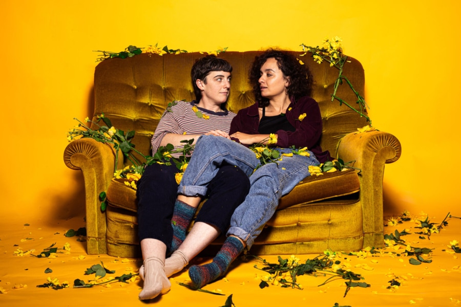 A couple sat on a sofa with flowers all over it. The girl has her legs over the boy's lap.