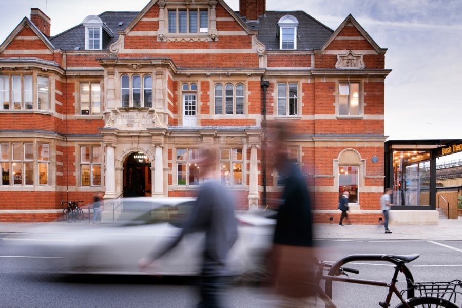 An image on a street. People are walking by and there is a car zooming past.