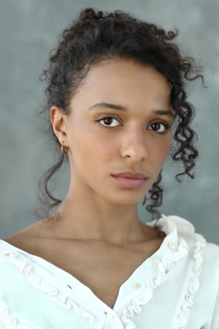 Tia Bannon headshot. She wears a white top and has curly brown hair.